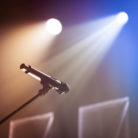 Low angle of professional microphone on stand placed on stage against bright colorful lights in concert hall