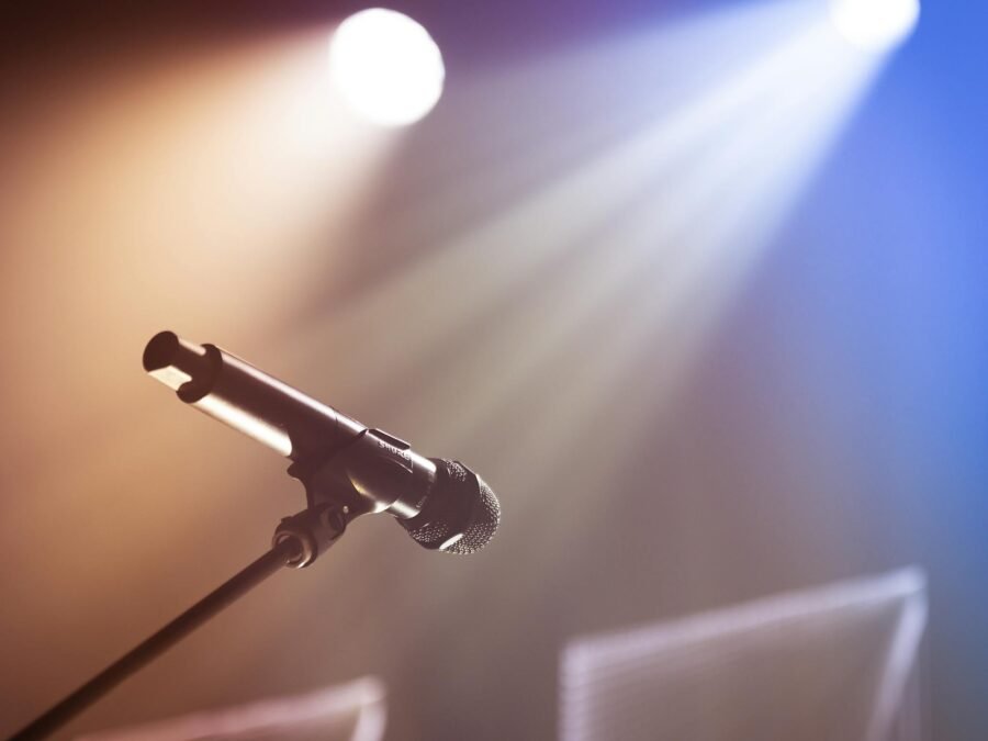 Low angle of professional microphone on stand placed on stage against bright colorful lights in concert hall